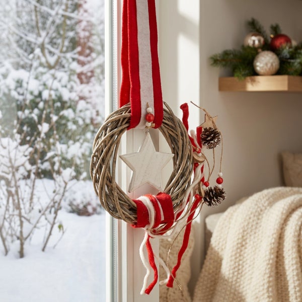 Weihnachtlicher Türkranz aus Weidengeflecht mit Sternanhänger und Dekobändern vor einem Fenster in winterlicher Umgebung.