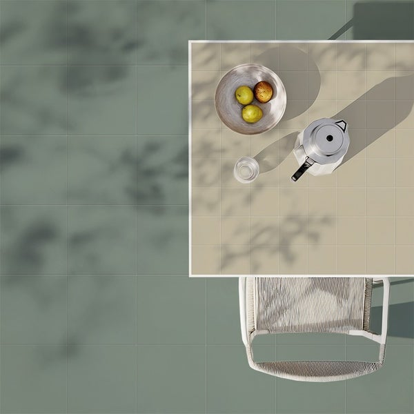 Draufsicht auf einen Terrassentisch mit Obstschale und Kaffeekanne auf quadratischen Bodenfliesen in zwei Kontrastfarben mit Schattenwurf.