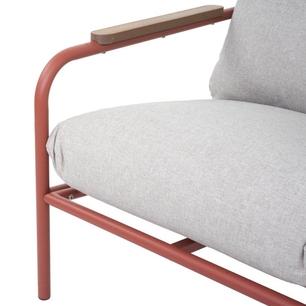 Nahaufnahme eines Loungesessels mit terrakottafarbenem Metallgestell, hellgrauen Stoffkissen und einer Armlehne aus Holz.
