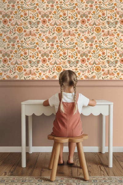 Kind sitzt an Schreibtisch vor einer Wand mit Blumentapete.