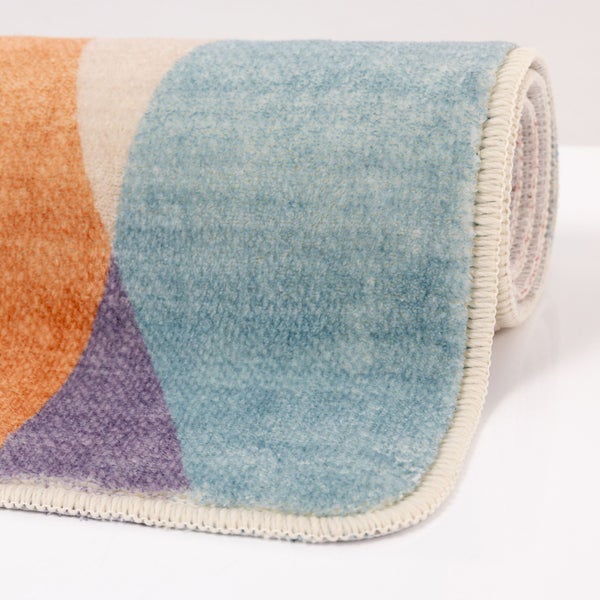 Aufgerollter Teppich mit weichem Flor und geometrischem Muster in Blau, Orange und Violett.
