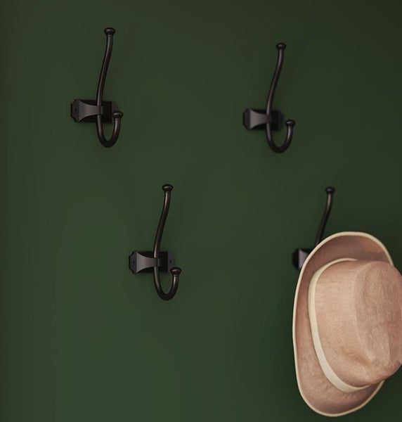 Vier Garderobenhaken an einer Wand, einer davon mit Hut