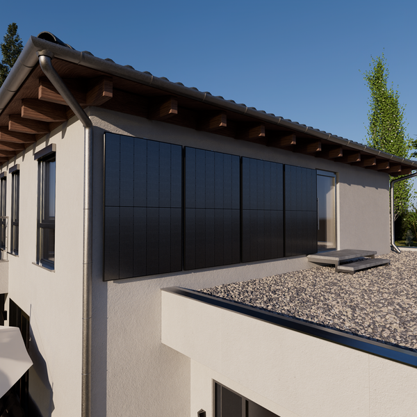 Vier schwarze Solarmodule an einer hellen Hauswand über einer Kiesfläche. Modernes Haus mit sichtbaren Holzbalken unter dem Dachüberstand.