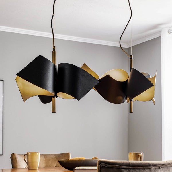 Moderne Pendelleuchte mit geschwungenen, bandförmigen Schirmen, außen schwarz und innen goldfarben, über einem Esstisch hängend.