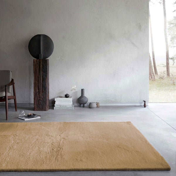 Hellbrauner rechteckiger Hochflor-Teppich in einem minimalistischen Raum mit Betonboden, Sessel und künstlerischen Dekorationsobjekten.
