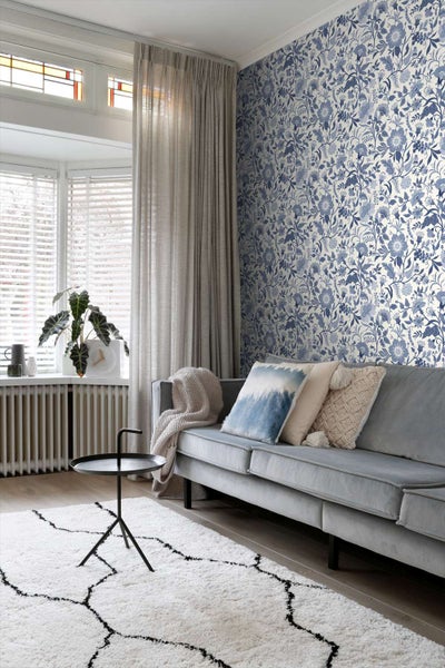 Wohnzimmer mit Vliestapete mit floralem Muster in hellen Tönen, ergänzt durch ein samtiges Sofa, Beistelltisch und gemusterten Teppich.
