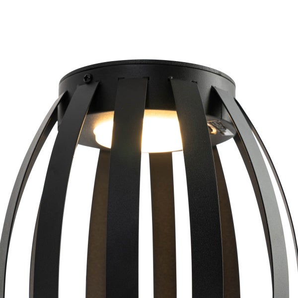 Detailaufnahme eines schwarzen Lampenschirms aus gebogenen Metalllamellen mit eingeschalteter Lichtquelle.