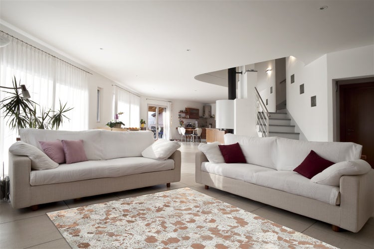 Helles offenes Wohnzimmer mit zwei Sofas und einem Teppich mit abstraktem Muster auf dem Fliesenboden vor einer offenen Küche und Treppe.