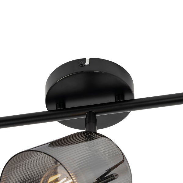 Detail einer schwarzen Deckenleuchte mit runder Halterung, Metallstange und einem geriffelten Strahler aus Rauchglas.