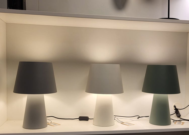 Drei moderne Tischleuchten mit konischem Fuß und Lampenschirm in einem Regal.