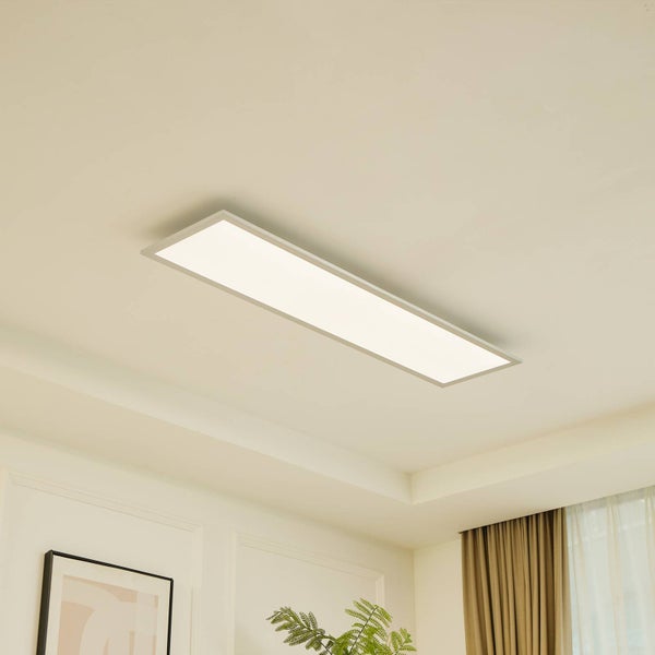 Rechteckiges, flaches LED-Panel an einer Decke in einem hellen, modern eingerichteten Raum mit Vorhängen und einer Pflanze.