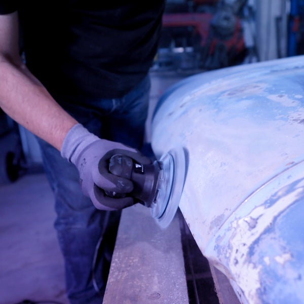 Eine Person schleift ein Autoteil mit einem Schleifgerät.