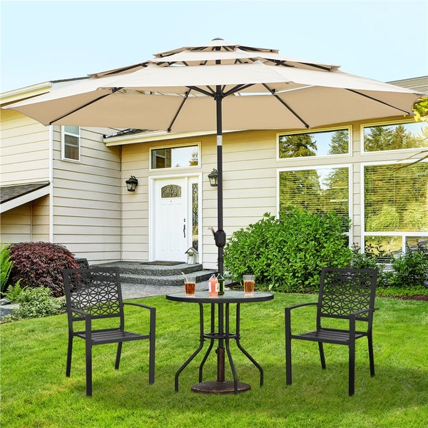 Gartenmöbel-Set auf Rasen mit zwei schwarzen Metallstühlen mit Muster, rundem Glastisch und großem beigen Sonnenschirm mit drei Stufen.