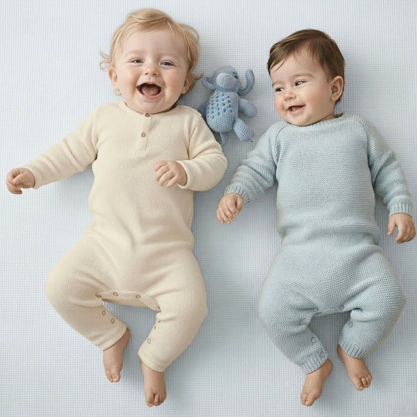 Zwei Babys in gestrickten Einteilern liegen auf einer strukturierten Matte, zwischen ihnen liegt ein kleines gestricktes Stofftier.