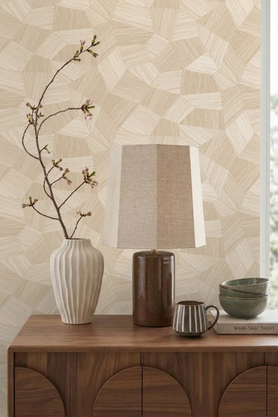 Vliestapete mit geometrischem Muster in Holzoptik auf einer Wand hinter einer Tischlampe und einer Vase auf einer Holzkommode.