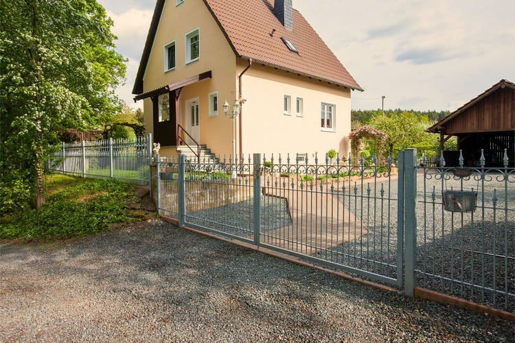 Hausansicht mit Metallzaun und Zufahrt