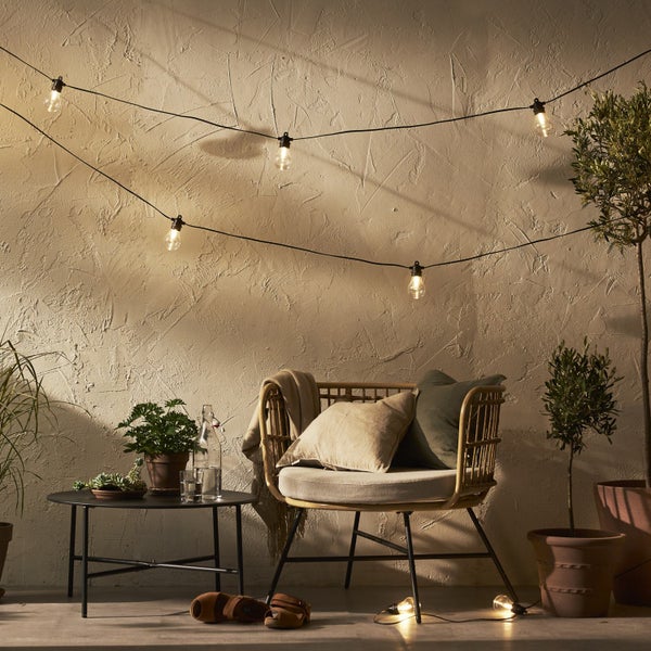 Szene mit Lichterkette, Sessel mit Kissen, Tisch, Pflanzen und Dekoration für den Außenbereich