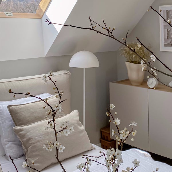 Helles Schlafzimmer im Dachgeschoss mit beigem Bett, weißer Stehlampe und Kommode unter einer Dachschräge.