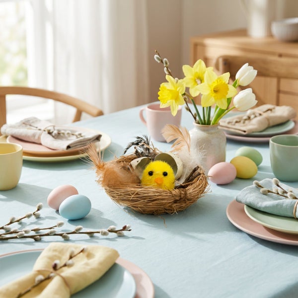 Festlich gedeckter Ostertisch mit einer Tischdekoration aus einem Vogelnest mit Küken, Ostereiern, Frühlingsblumen und Pussyweidenzweigen.