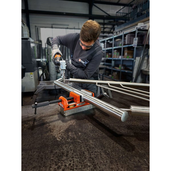 Ein Handwerker bearbeitet ein Metallrohr mit einer Bandsäge, das in einem Schraubstock eingespannt ist.