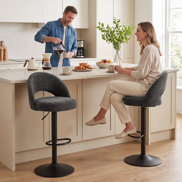 Ein Paar höhenverstellbare Barhocker mit gepolsterter Sitzschale in einer hellen, modernen Küche mit Kochinsel und zwei Personen.