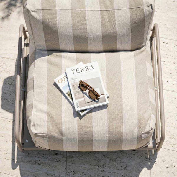 Draufsicht auf einen Garten-Lounge-Sessel mit beige-weiß gestreiftem Sitzkissen, Metallgestell, Zeitschriften und einer Sonnenbrille.