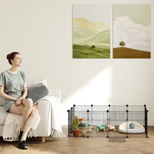 Schwarzer Welpenauslauf aus Metall in einem hellen Wohnzimmer mit Sofa, Landschaftsbildern und Parkettboden.