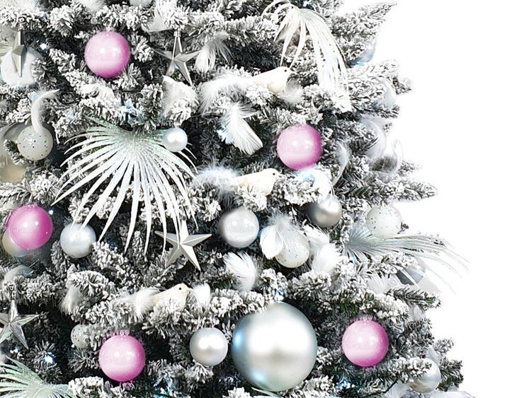 Detailansicht eines künstlichen, verschneiten Weihnachtsbaums mit Dekoration aus Christbaumkugeln, Sternen, Federn und Vogelornamenten.