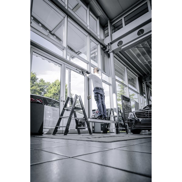 Mann reinigt Fenster auf einer Arbeitsbühne in einem hellen Raum.