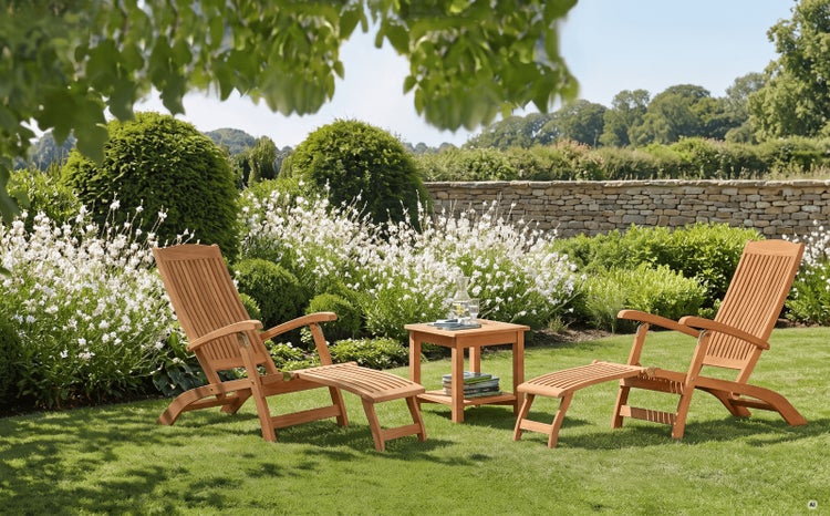 Gartenmöbel-Set aus Holz mit zwei Liegestühlen, Fußstützen und einem Beistelltisch auf einem Rasen in einem hellen Garten.