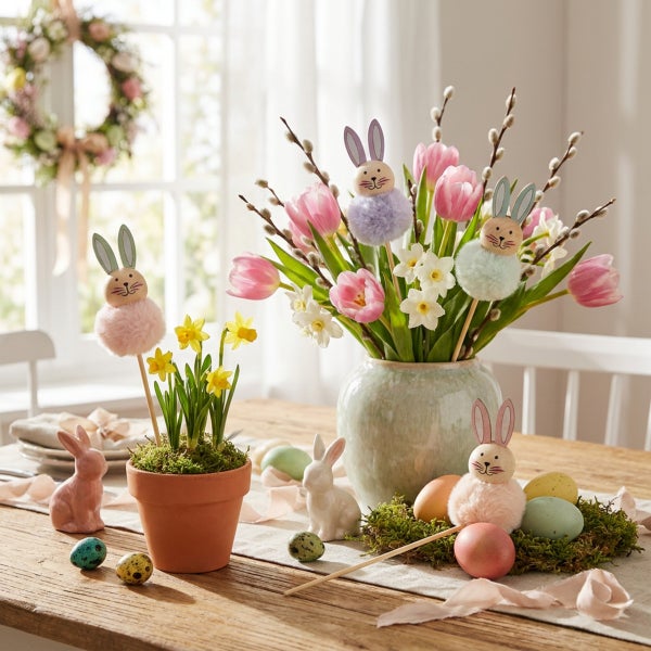 Osterdekoration mit Blumenstrauß, blühenden Narzissen im Tontopf, Hasenfiguren und Ostereiern auf einem Holztisch als frühlingshafte Tischdeko.