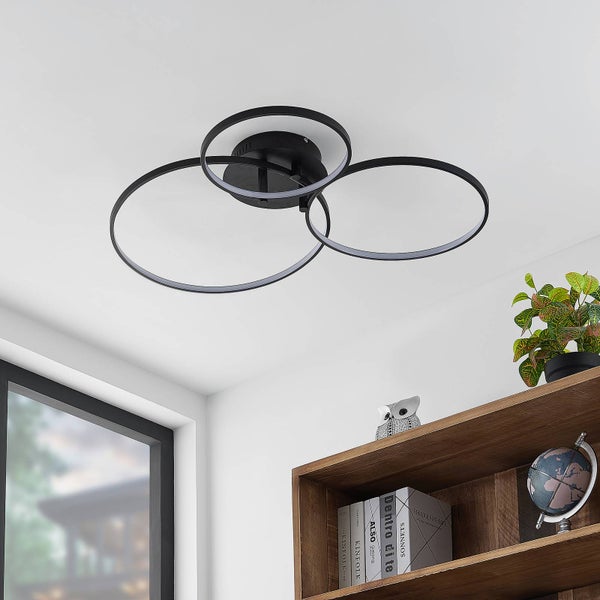 Nahaufnahme der runden schwarzen Deckenhalterung einer Deckenleuchte mit geschwungenen Metallarmen.