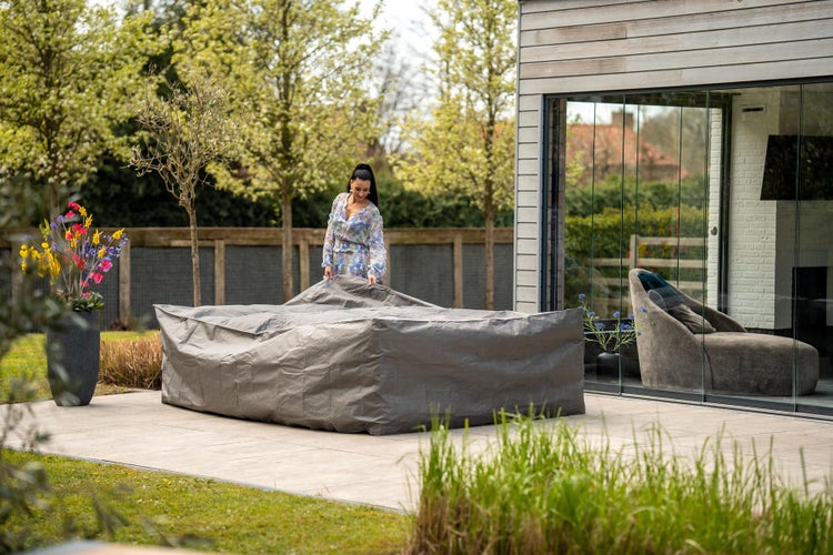 Eine Frau deckt eine Sitzgruppe im Garten mit einer Schutzhülle ab.