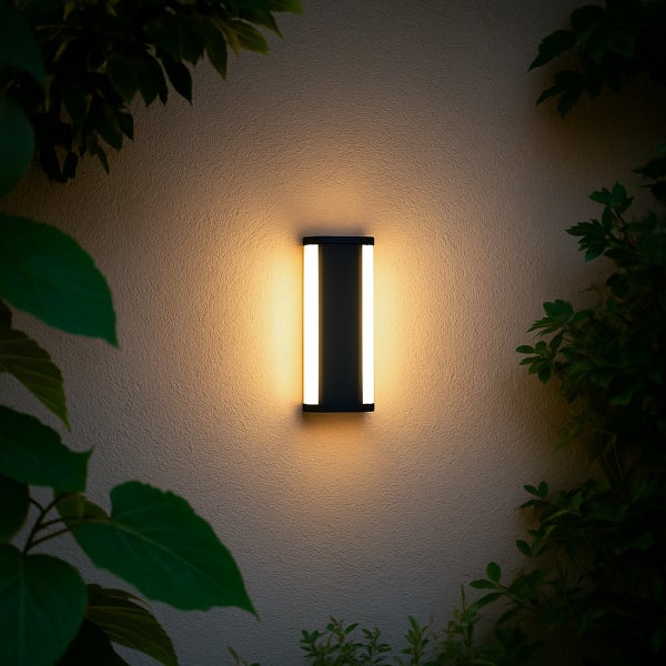 Moderne rechteckige LED-Außenwandleuchte an einer strukturierten Wand zwischen Pflanzen, die warmes Licht abgibt.