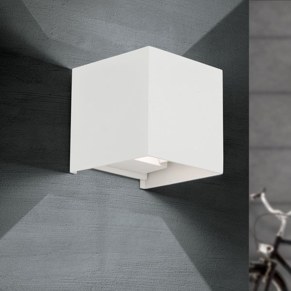 Würfelförmige Außenwandleuchte in Weiß mit Lichtkegeln nach oben und unten an einer Wand.