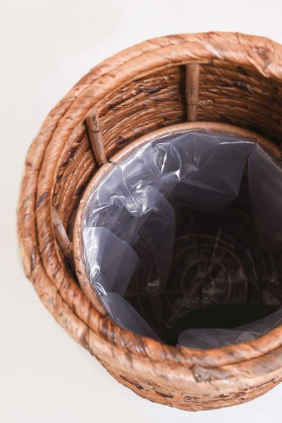 Ein runder Pflanzkorb aus geflochtenem Naturmaterial mit einer transparenten Kunststoffeinlage.