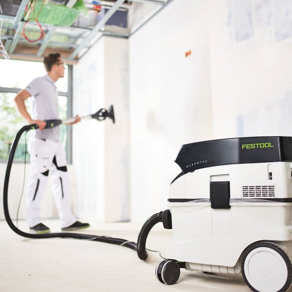 Ein Handwerker schleift eine verputzte Wand mit einem Festool Langhalsschleifer, der an ein Festool Absaugmobil angeschlossen ist.
