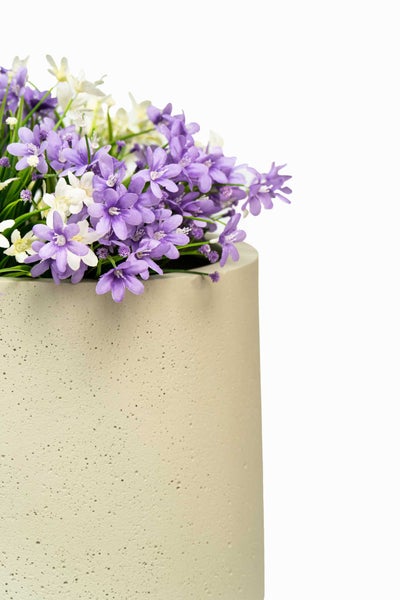 Zylindrischer Pflanztopf mit strukturierter Oberfläche in Betonoptik, bepflanzt mit violetten und weißen Kunstblumen.