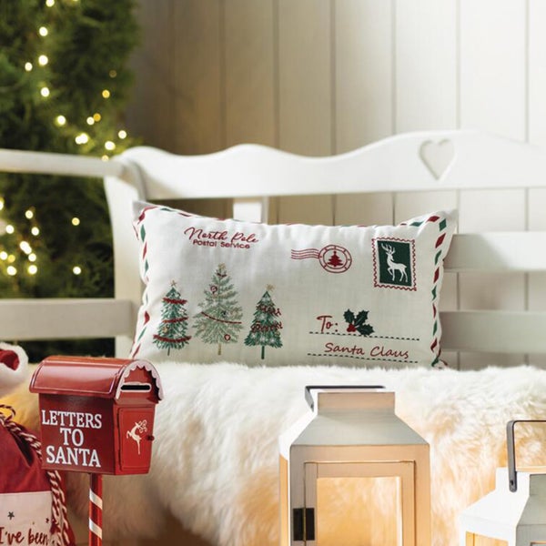 Weihnachtskissen mit weihnachtlichem Brief-Motiv auf einer Bank mit Lichterkette und Dekoration.