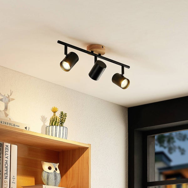 Dreiflammiger Deckenstrahler aus schwarzem Metall und Holz, montiert an einer Decke über einem Holzregal mit Dekoration.