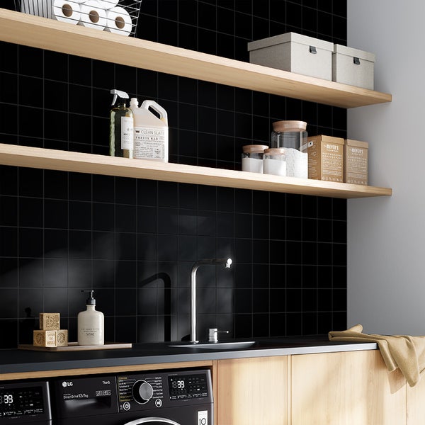 Moderne Waschküche mit schwarzen quadratischen Fliesen an der Wand, hellen Holzregalen, Waschmaschine und einer Spüle mit Wasserhahn.