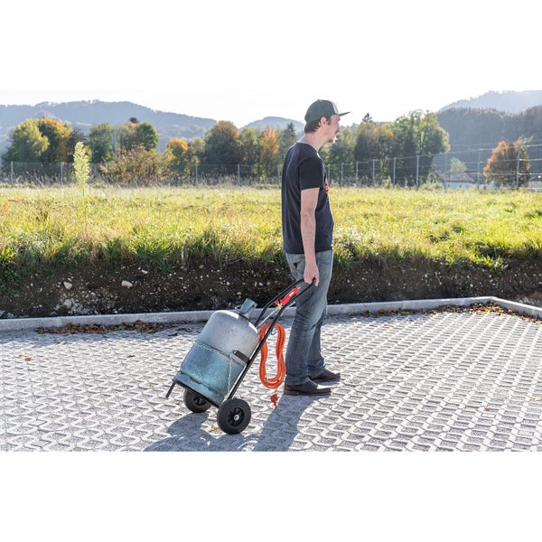 Eine Person zieht einen Transportwagen mit Gasflasche und Gasschlauch im Freien.