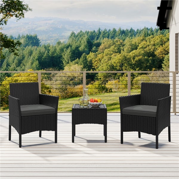 Gartenmöbel-Set mit zwei Korbsesseln, grauen Kissen und einem Tisch mit Glasplatte auf einer Terrasse mit Landschaftsblick