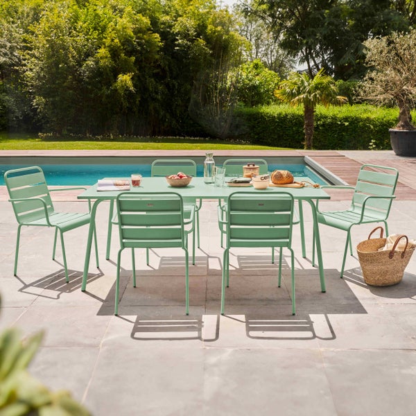 Garten-Essgruppe mit einem rechteckigen Metalltisch und sechs passenden Stühlen in Hellgrün, auf einer Steinterrasse neben einem Swimmingpool.
