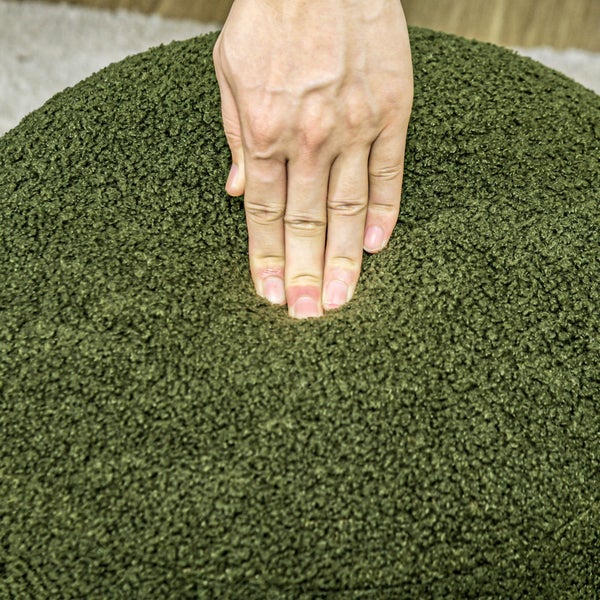 Hand drückt in einen grünen Sitzpouf mit Teddyplüschbezug.