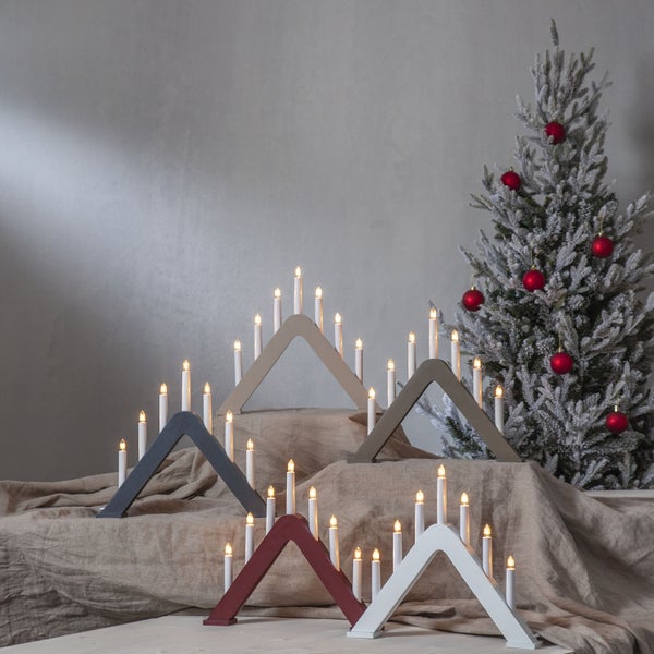 Dekorative Dreiecksleuchten mit LED-Kerzen auf Stofftisch mit Weihnachtsbaum im Hintergrund.