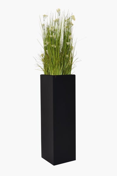 Künstliches Gras mit weißen Blüten in einem hohen, quadratischen Pflanzgefäß in Schwarz.