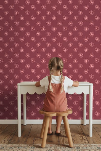 Kind sitzt an einem Kindertisch vor einer Wand mit Sonnen- und Mondtapete.