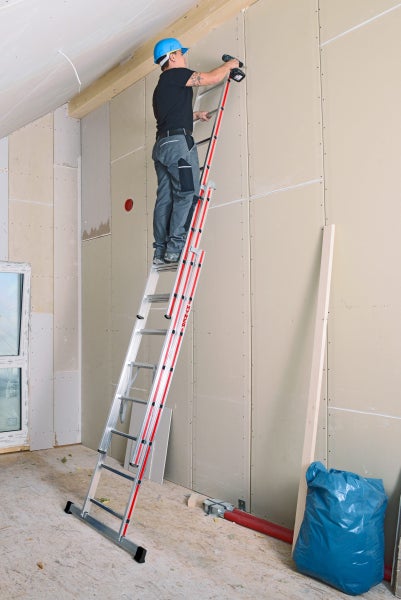Handwerker auf einer Mehrzweckleiter bei der Installation von Trockenbauwänden in einem Dachgeschoss.