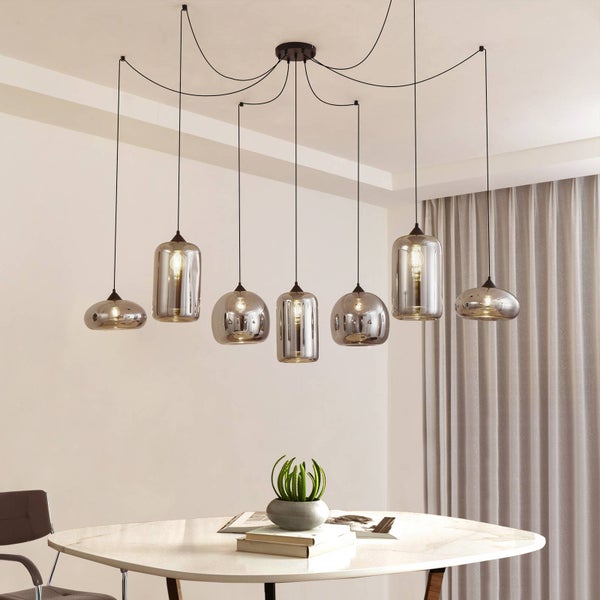 Siebenflammige Pendelleuchte mit rauchfarbenen Glasschirmen in verschiedenen Formen über einem Esstisch in einem modernen, hellen Raum.